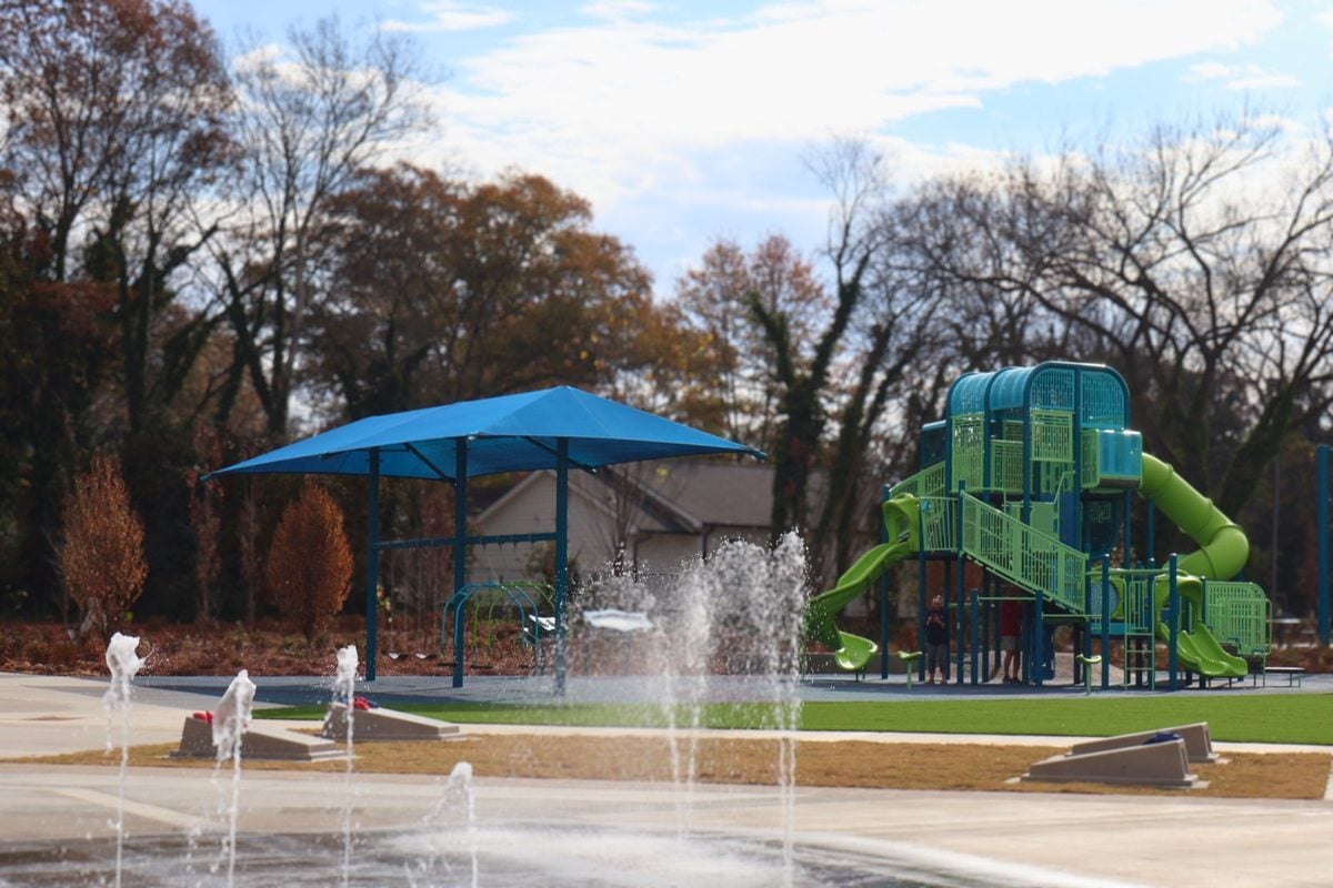 Water jets arc over the splash pad at Banty Jones Park, with a green and teal play structure beyond