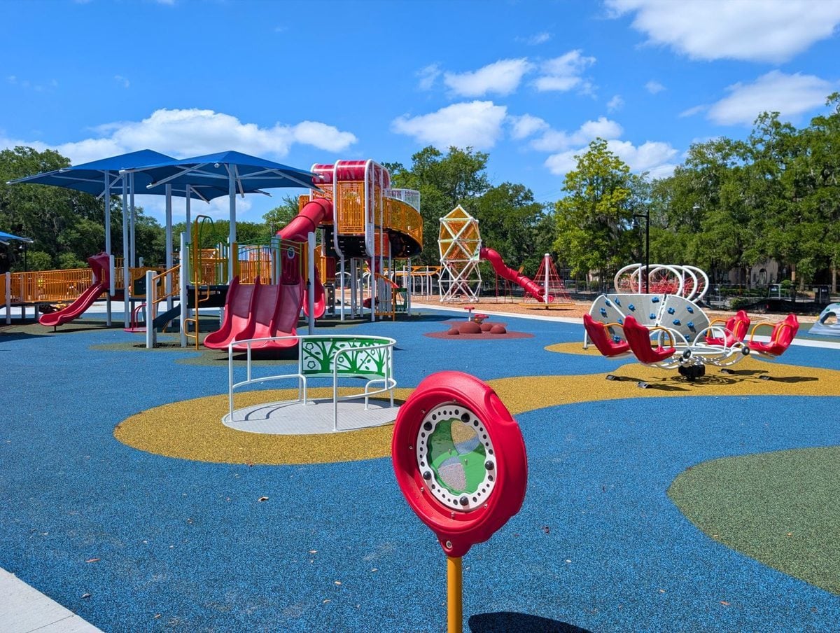 Red slides and shaded play structures at Daffin Signature Park, on blue, yellow and green poured surfacing