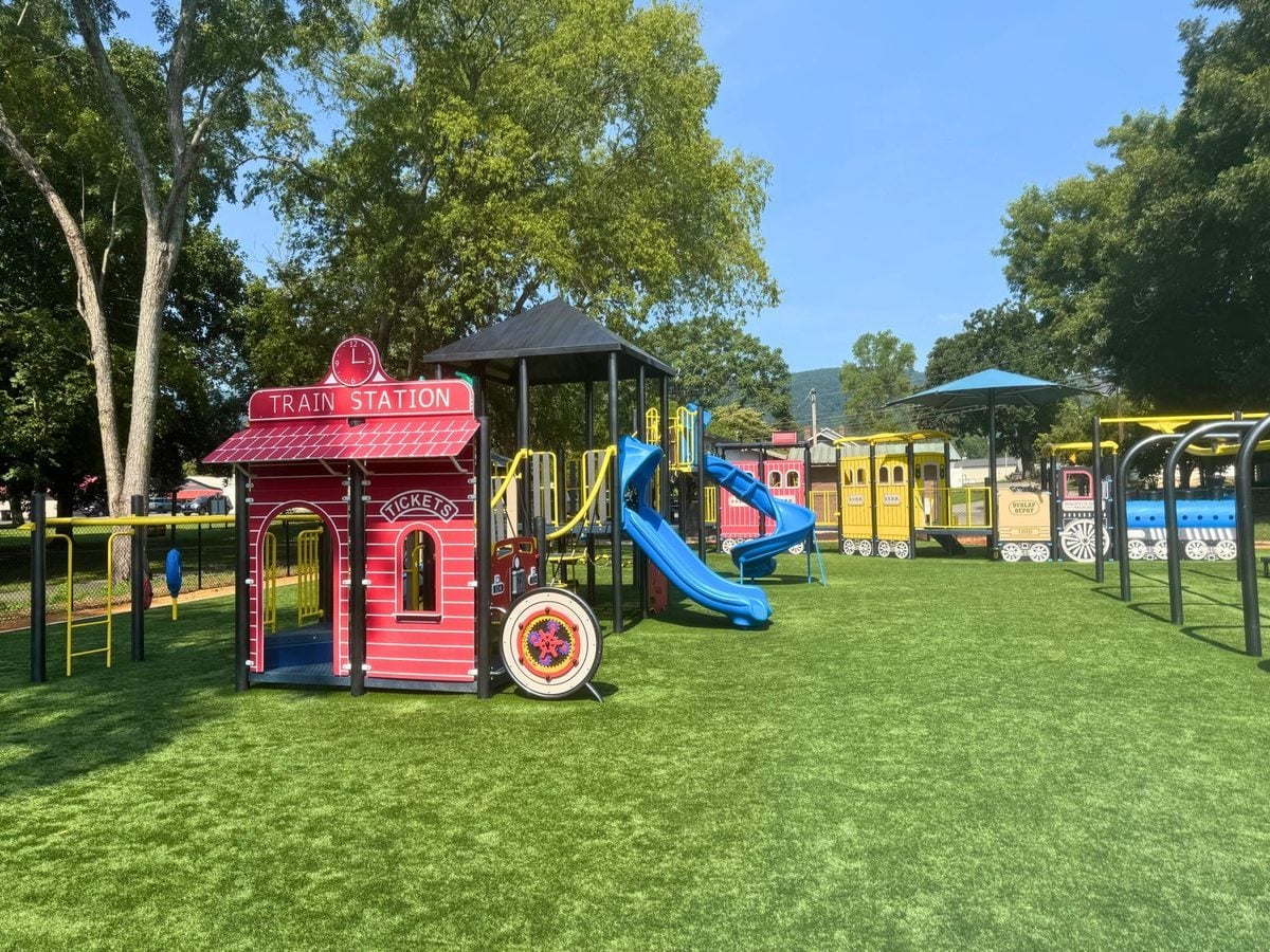 Train-themed playground at Harris Park, with a red train-station playhouse, blue slides and yellow train cars on synthetic turf