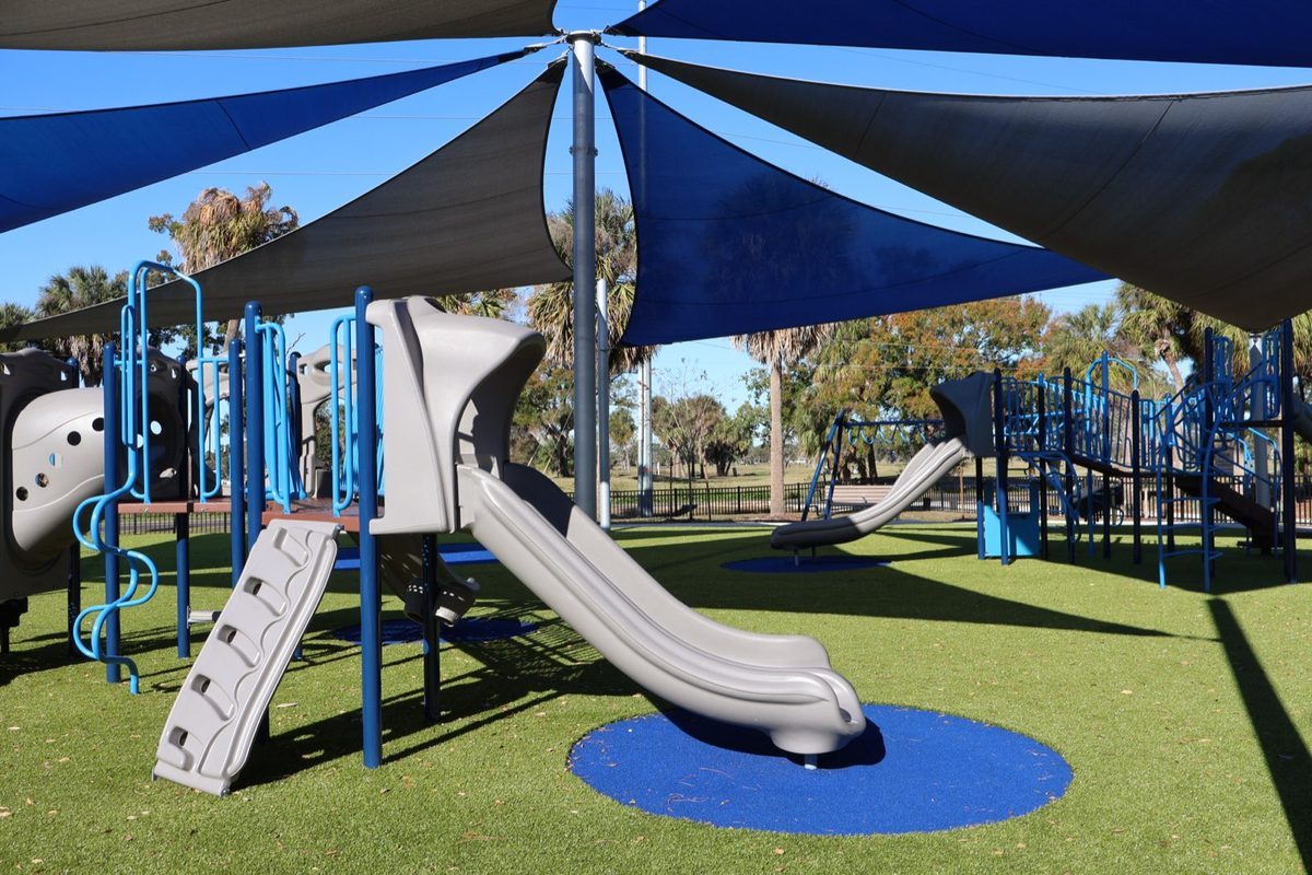 Blue sail shades over slides and climbers at Skyway Park, set on synthetic turf with poured safety circles